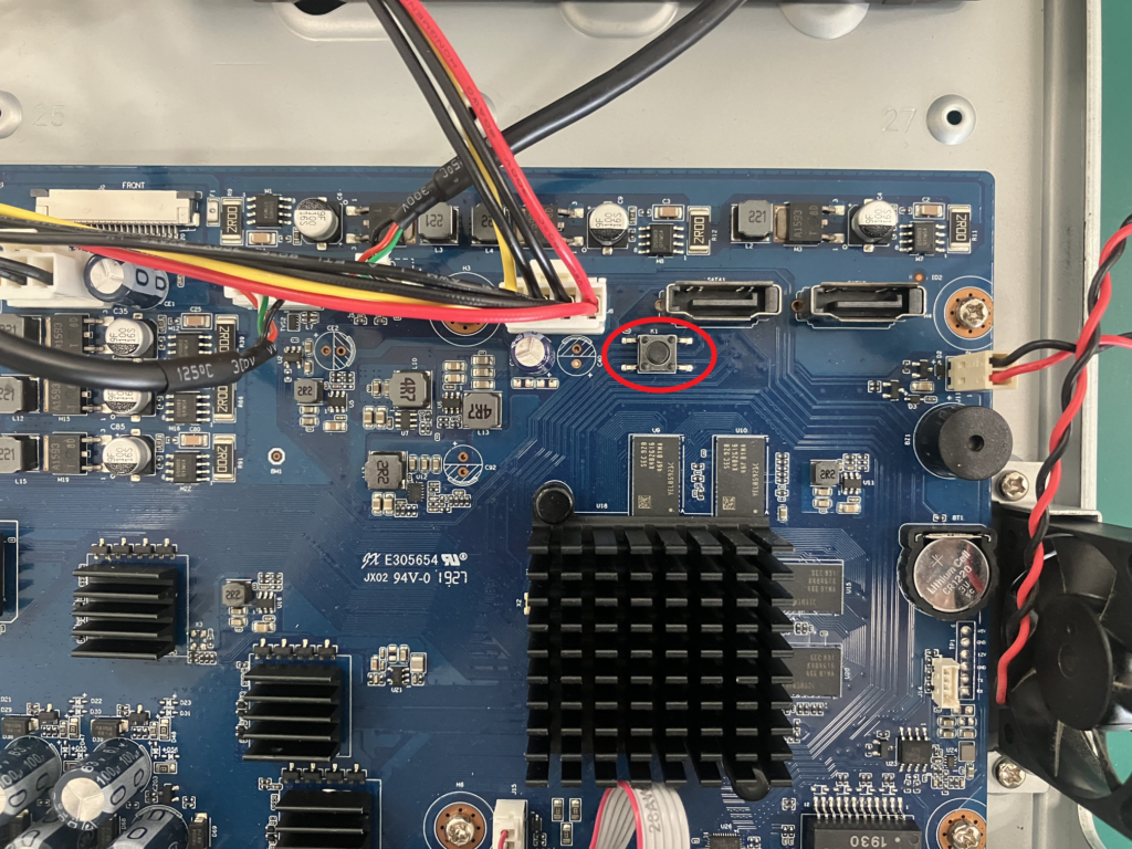 写真は:Dahuaのレコーダーをファクトリーリセットするためのボタンの位置の例を図示しています。フロントパネルを外し基板上のボタンを押下する必要があります。